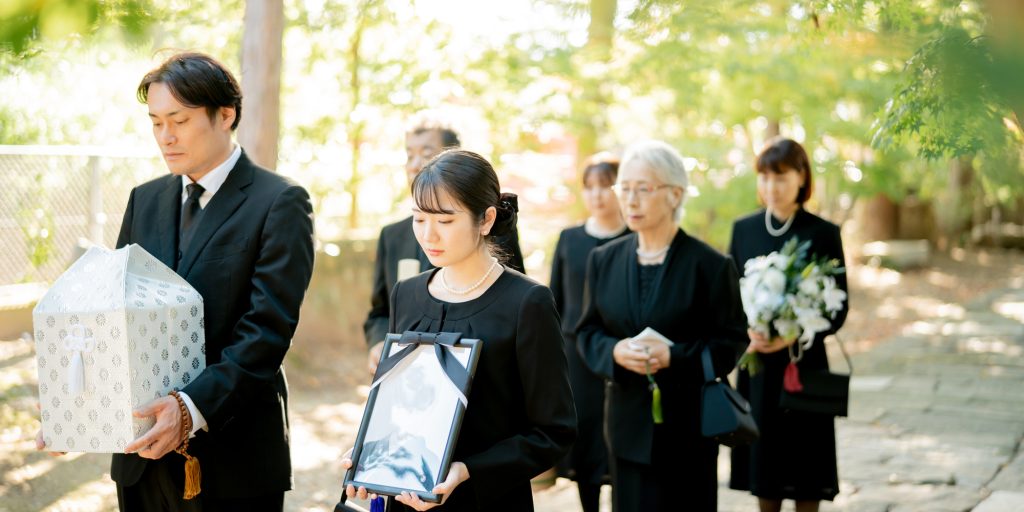 遺影と骨壺をもって歩く遺族